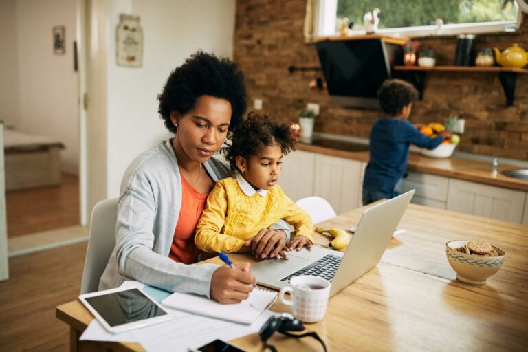 Woman holding a child on her lap while she works on a laptop