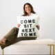 AliceAnne Loftus holding a pillow that reads, "Come sit next to me"