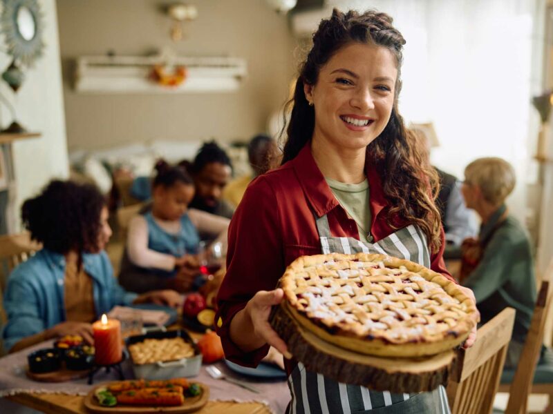 Woman holding a pie in front of a group of people at a table. Success is not pie! There's plenty to go around.