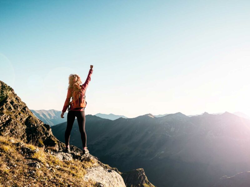 Woman standing on top of a mountain with her arm raised